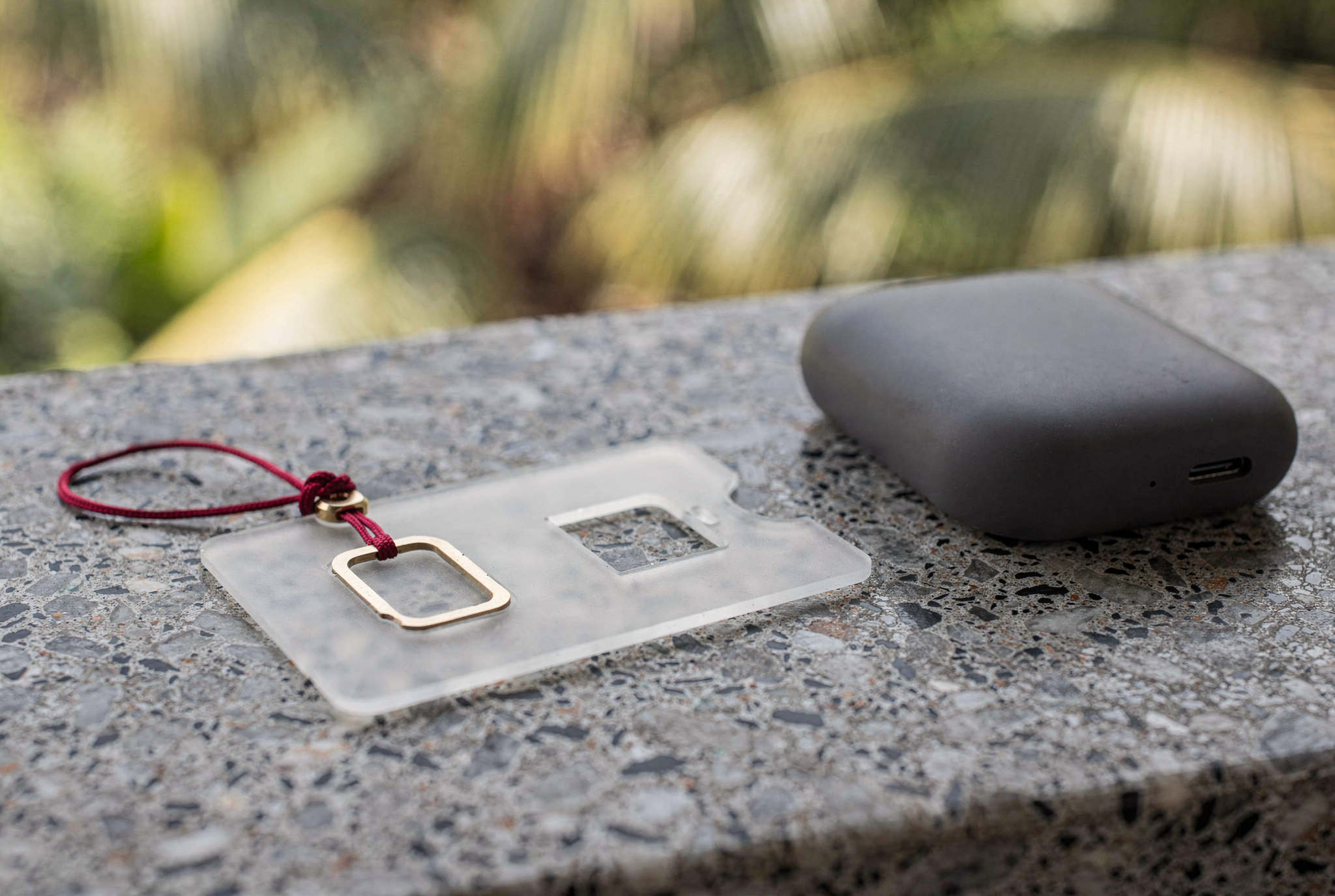 A clear plastic SIM card carrier and a brass ejector tool with a red cord resting on a terrazzo surface.