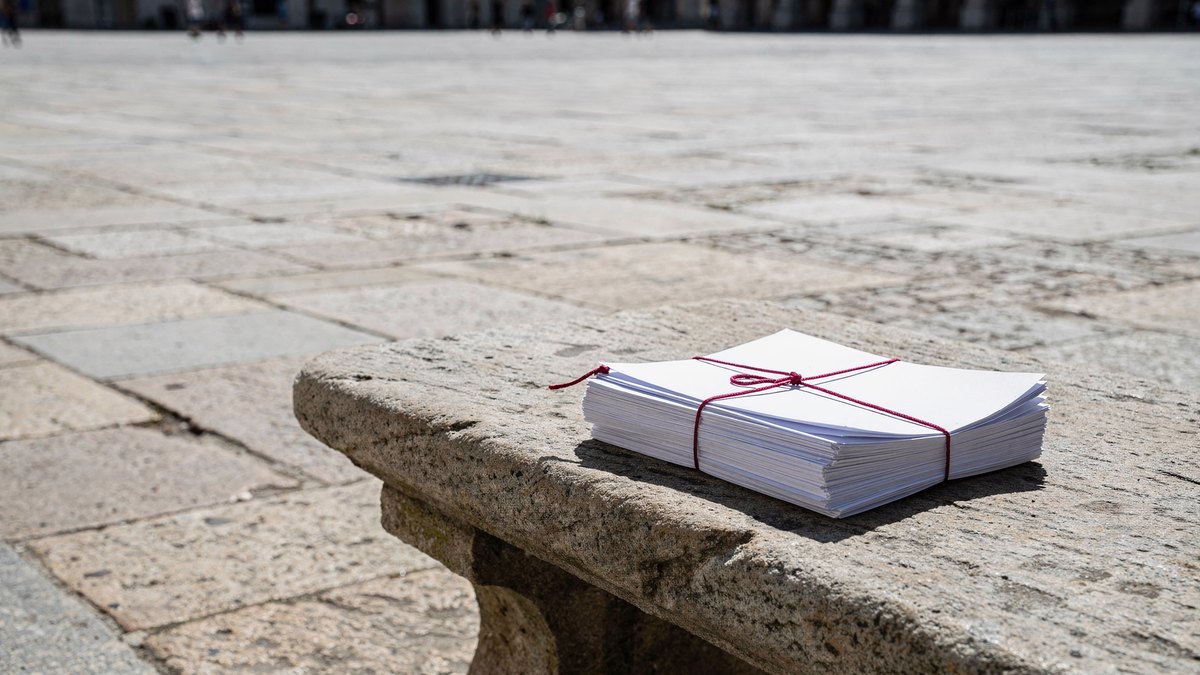 A solitary sheaf of papers tied with red twine sits on a large stone bench in an empty sunlit courtyard.
