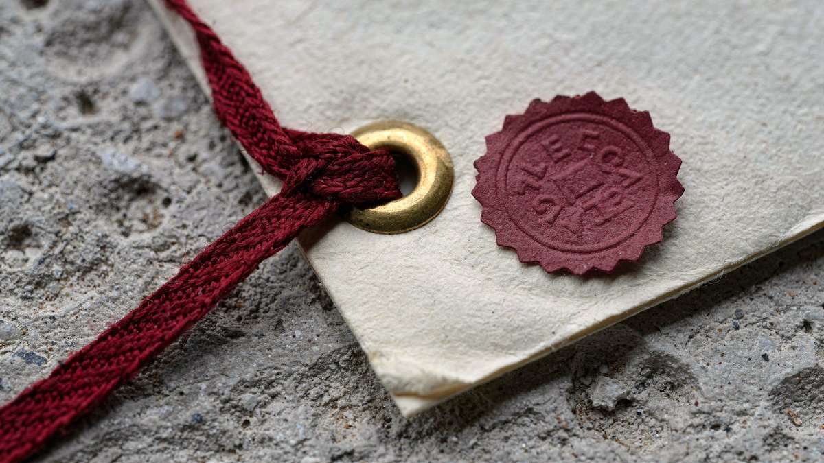 Close-up photograph of a red legal ribbon threaded through a brass grommet on heavy parchment sealed on a stone ledge.