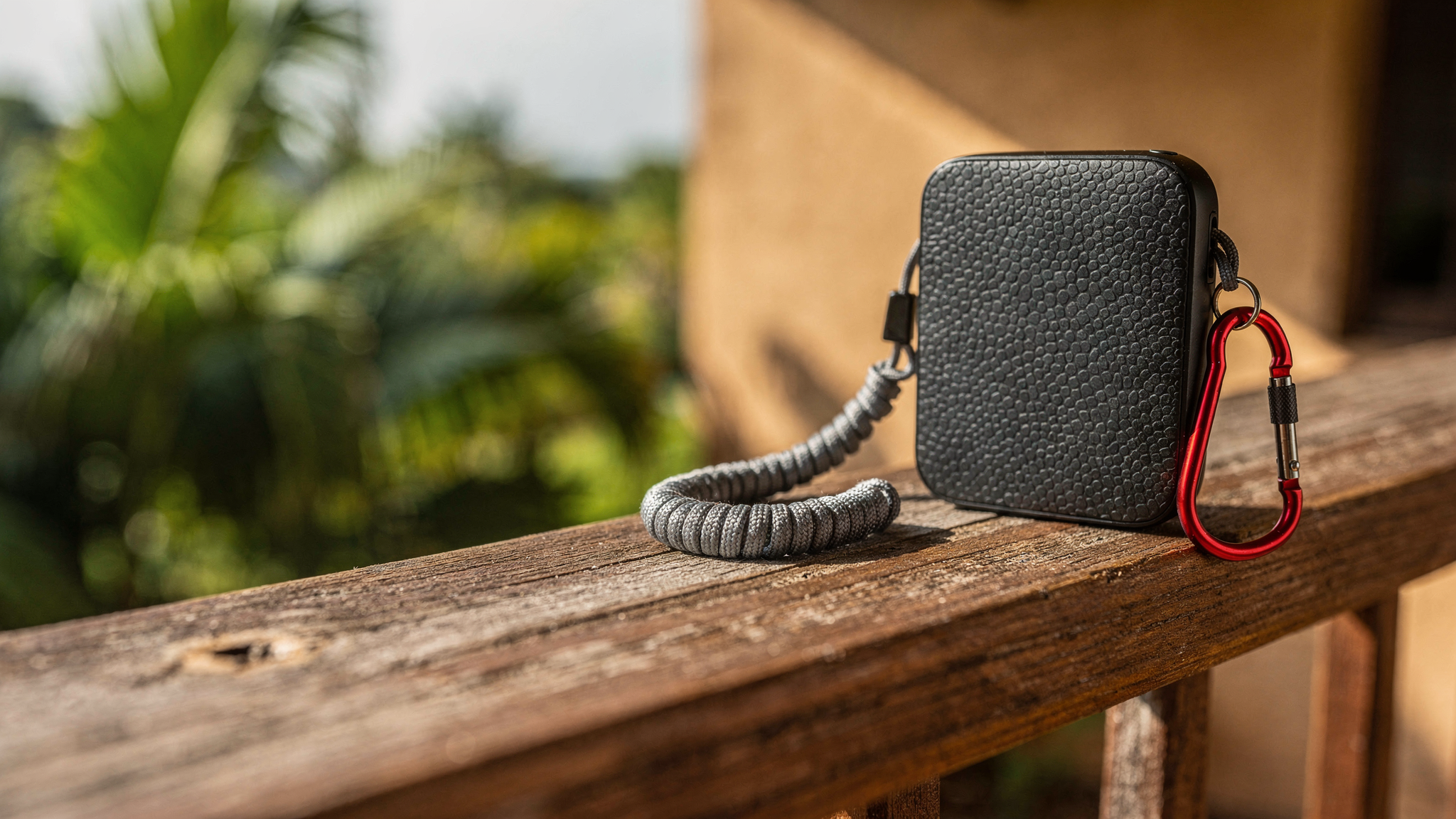 A compact black portable Wi-Fi router and red carabiner clip rest on a weathered teak railing outdoors.