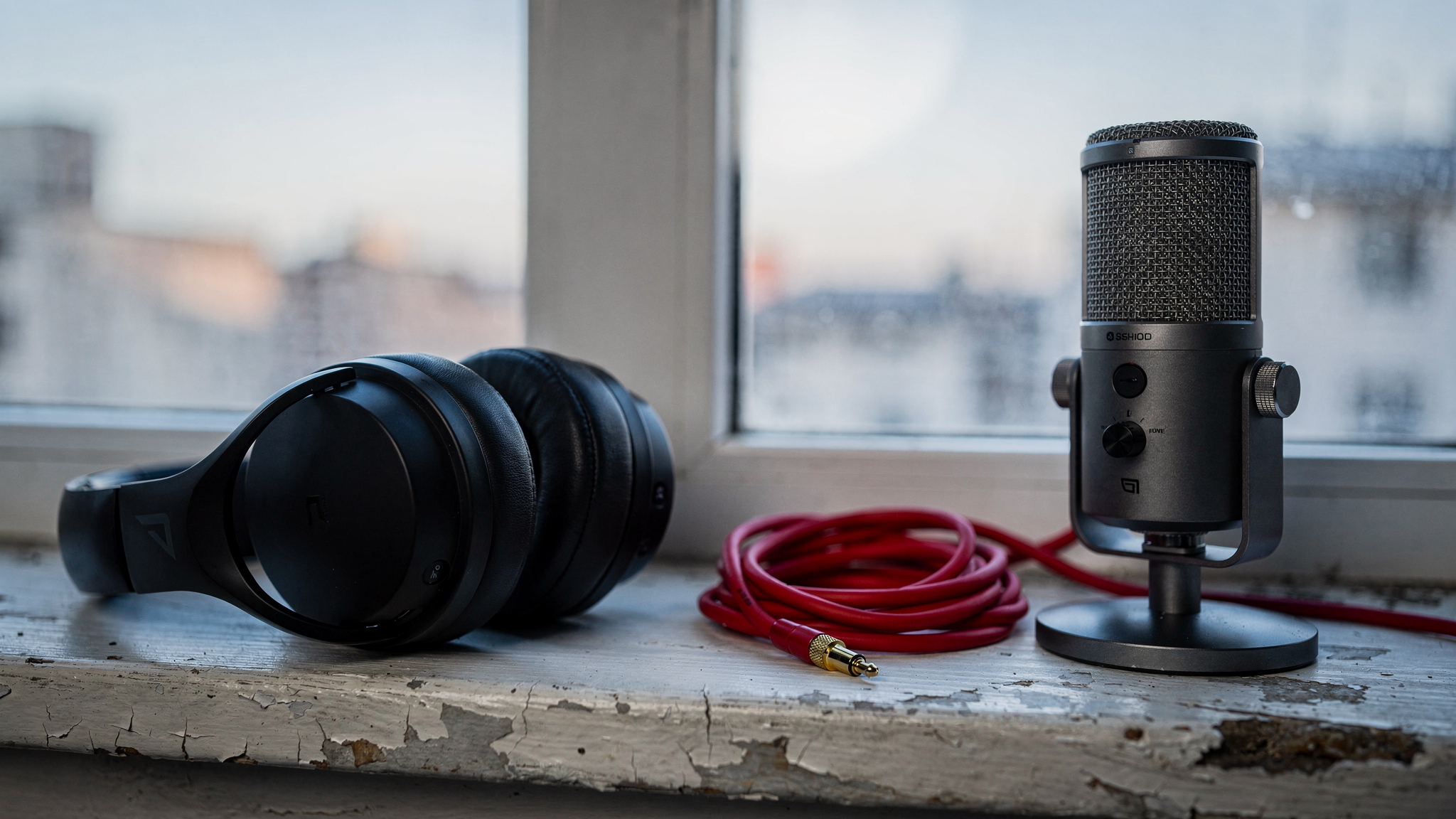 A pair of folded black monitor headphones and a compact desktop microphone resting on a concrete windowsill in morning light.