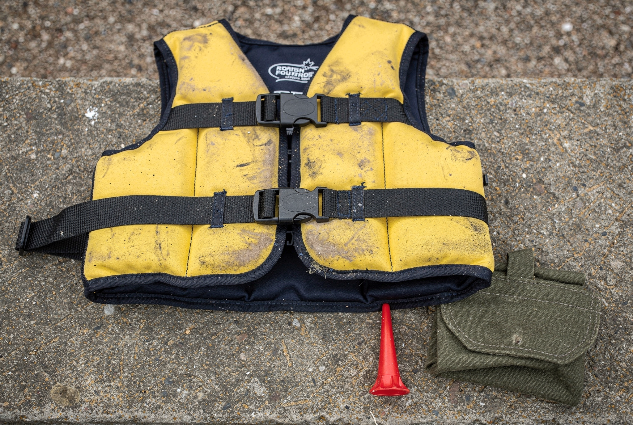 A worn children's swim vest, folded canvas pouch, and a small red diagnostic ear tip resting on a stone surface.