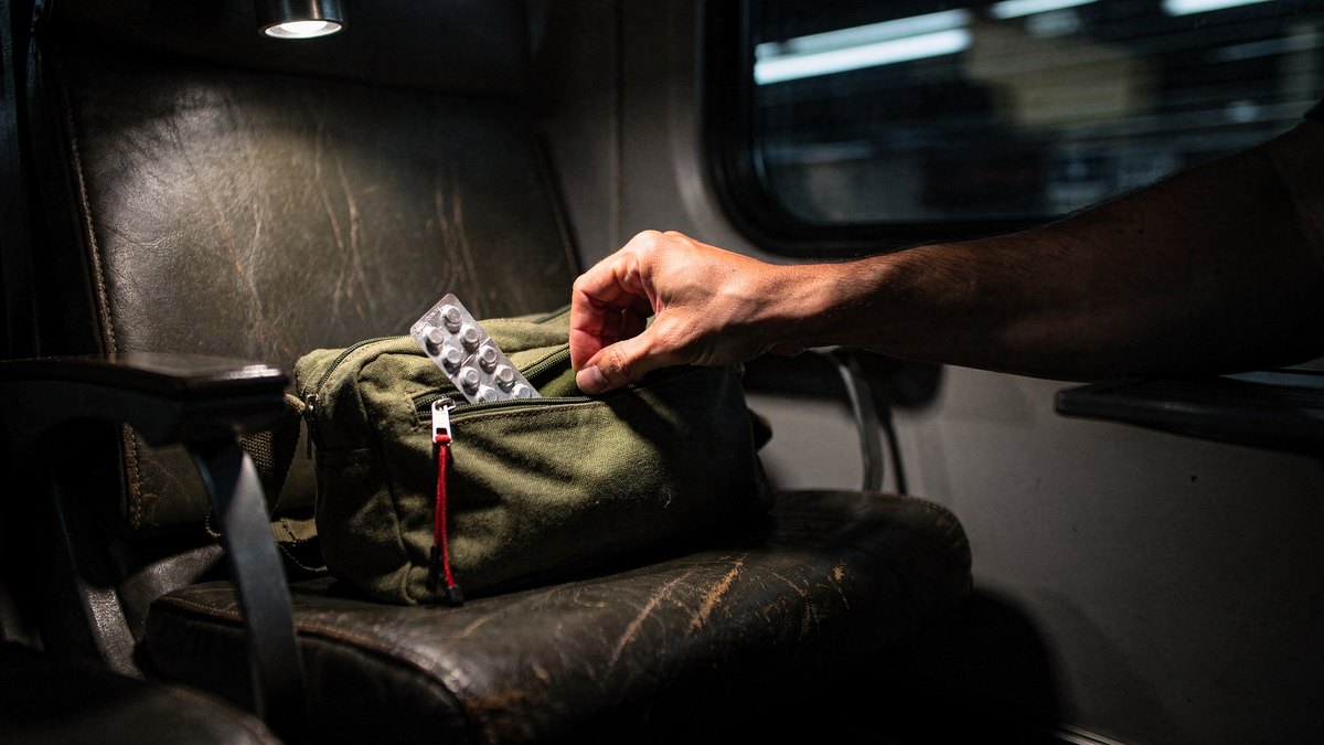 A traveler's hand reaches into a canvas organizer pouch under a single overhead night light on a moving train.