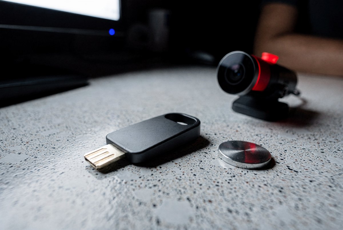 A hardware security key and aluminium seal token resting on a laminate counter under the sterile glow of a computer screen in the dark.